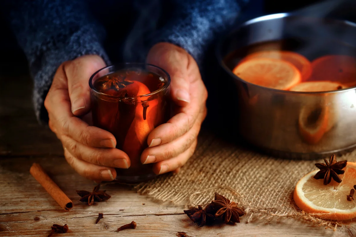 Older female hands holding a glass mug with hot mulled wine