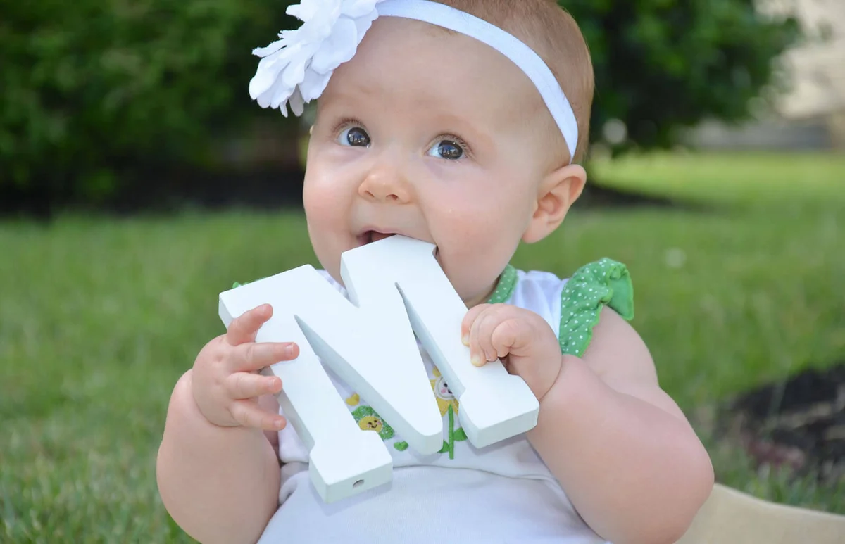 Cute baby girl tastes the large white wooden M