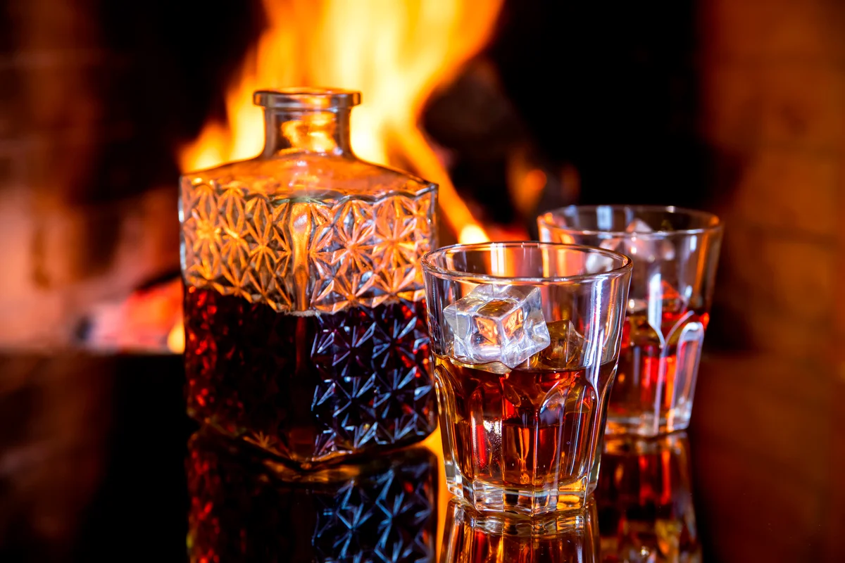 Two glasses and a of whiskey near the fireplace
