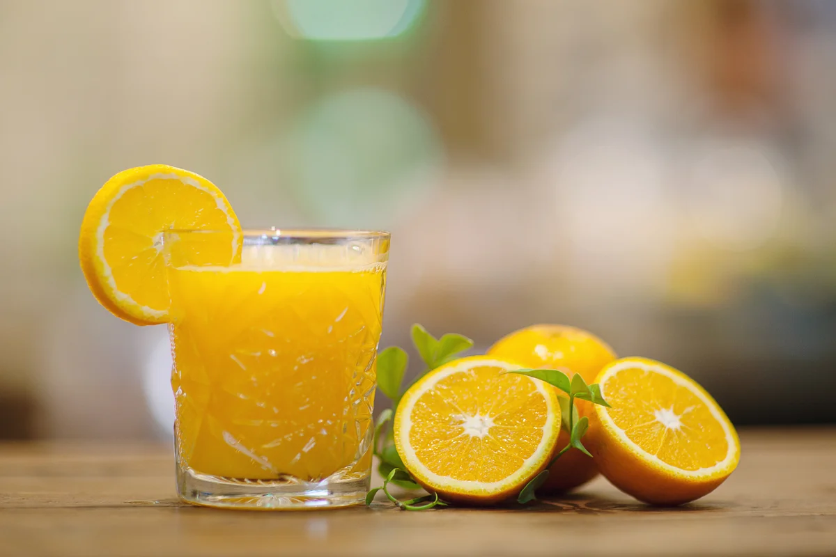 Brandy and fresh orange juice next to some orange slices on wooden table