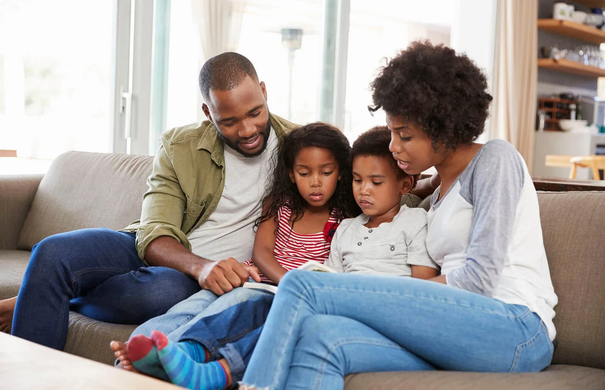 Family Sitting On Sofa In Lounge Reading Book Together