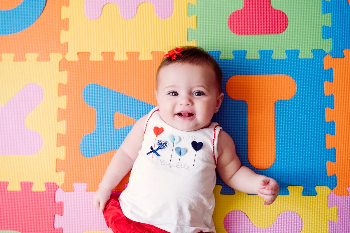 Cute baby girl relaxing on colorful alphabetical puzzle playmat