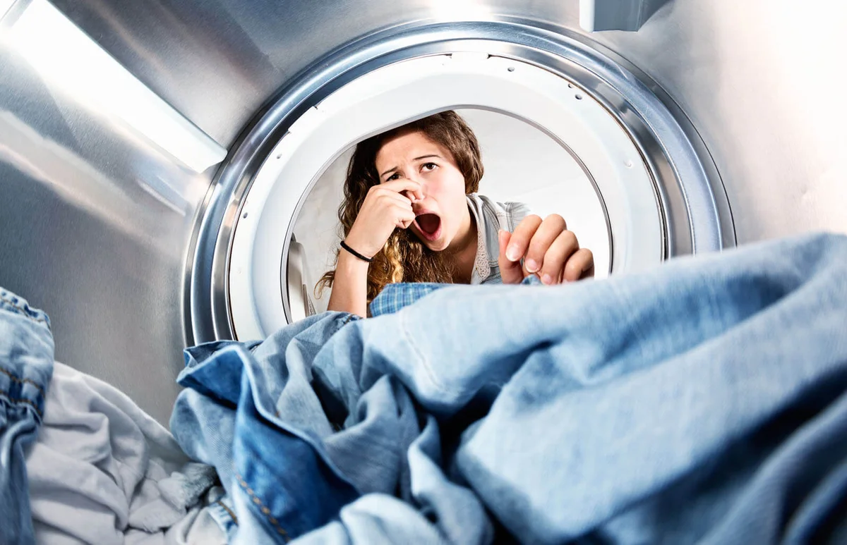 woman holding her nose as she looks at the laundry which must have been forgotten and now smells