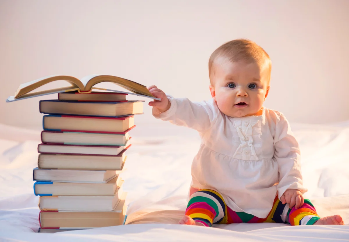 Baby sitting in bed with stack of books
