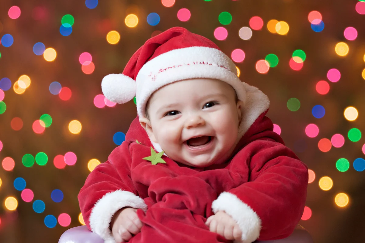 Smiley baby girl in a Santa Claus costume with a holiday lights colorful background