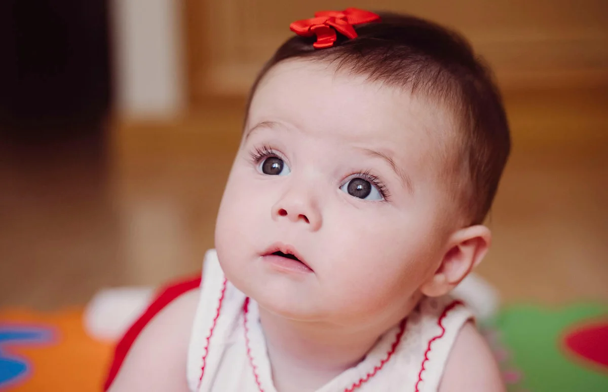 cute baby girl with red hair clip looking away while lying at home