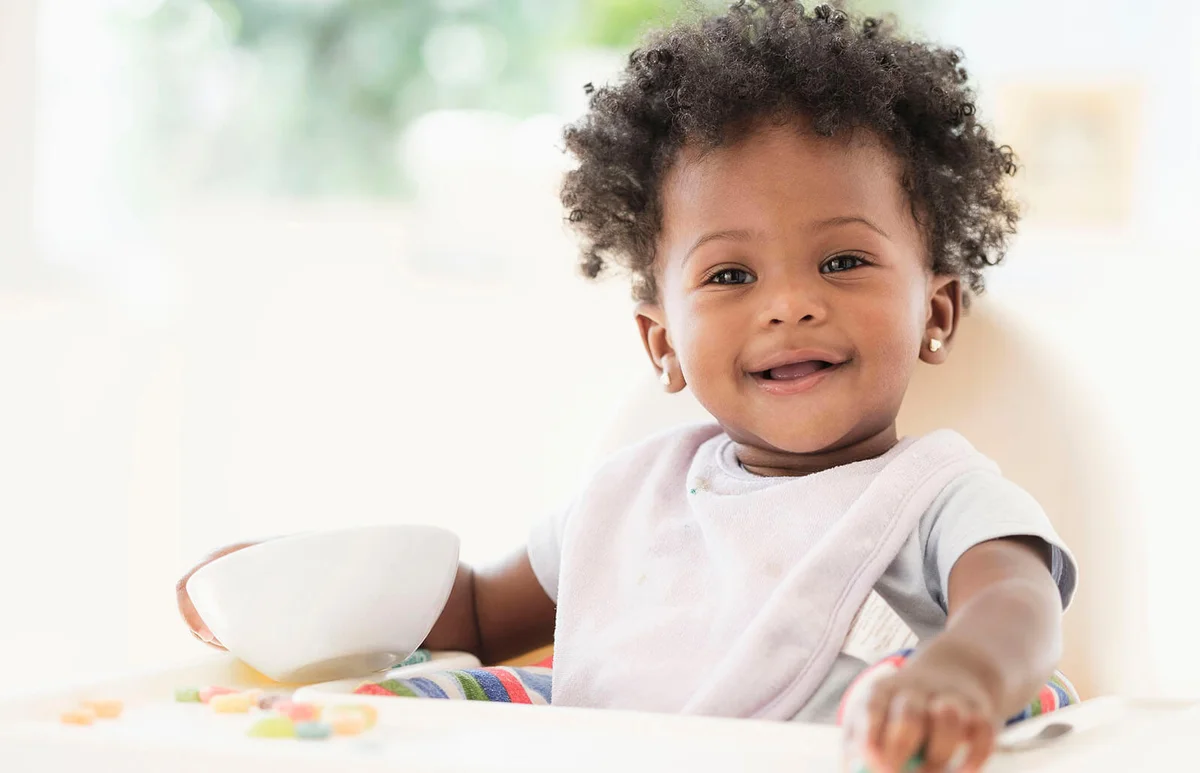 baby girl eating cereal from bowl in high chair