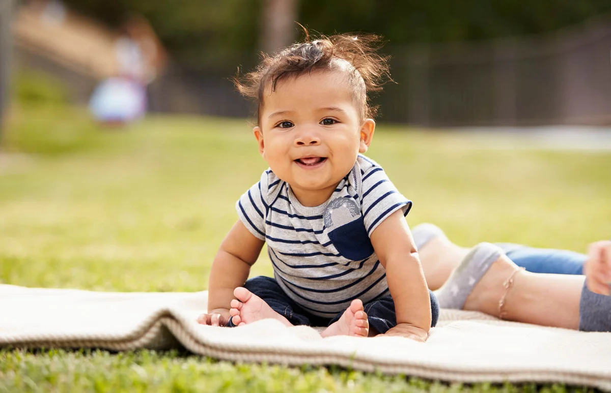 Little baby boy sitting up on a blanket in the park looking to camera
