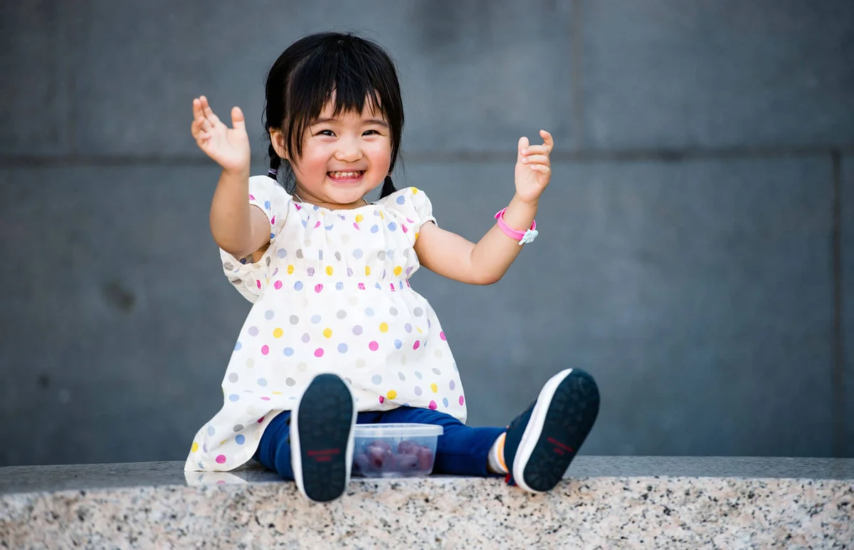 Toddler girl clapping hands on stone bench smiling