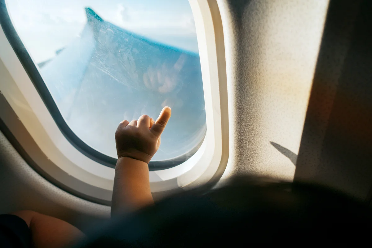 Hand of a toddler pointing airplane window against blue sky while travelling