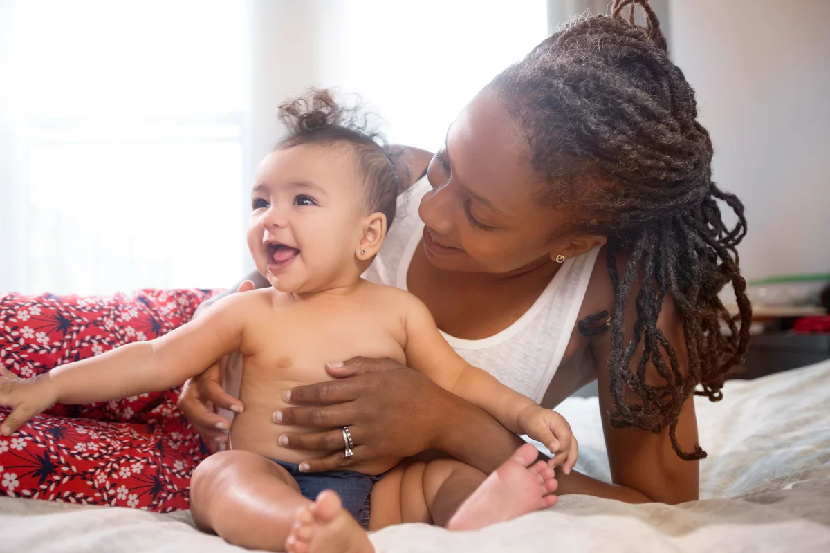 Mother holding smiling baby daughter on bed