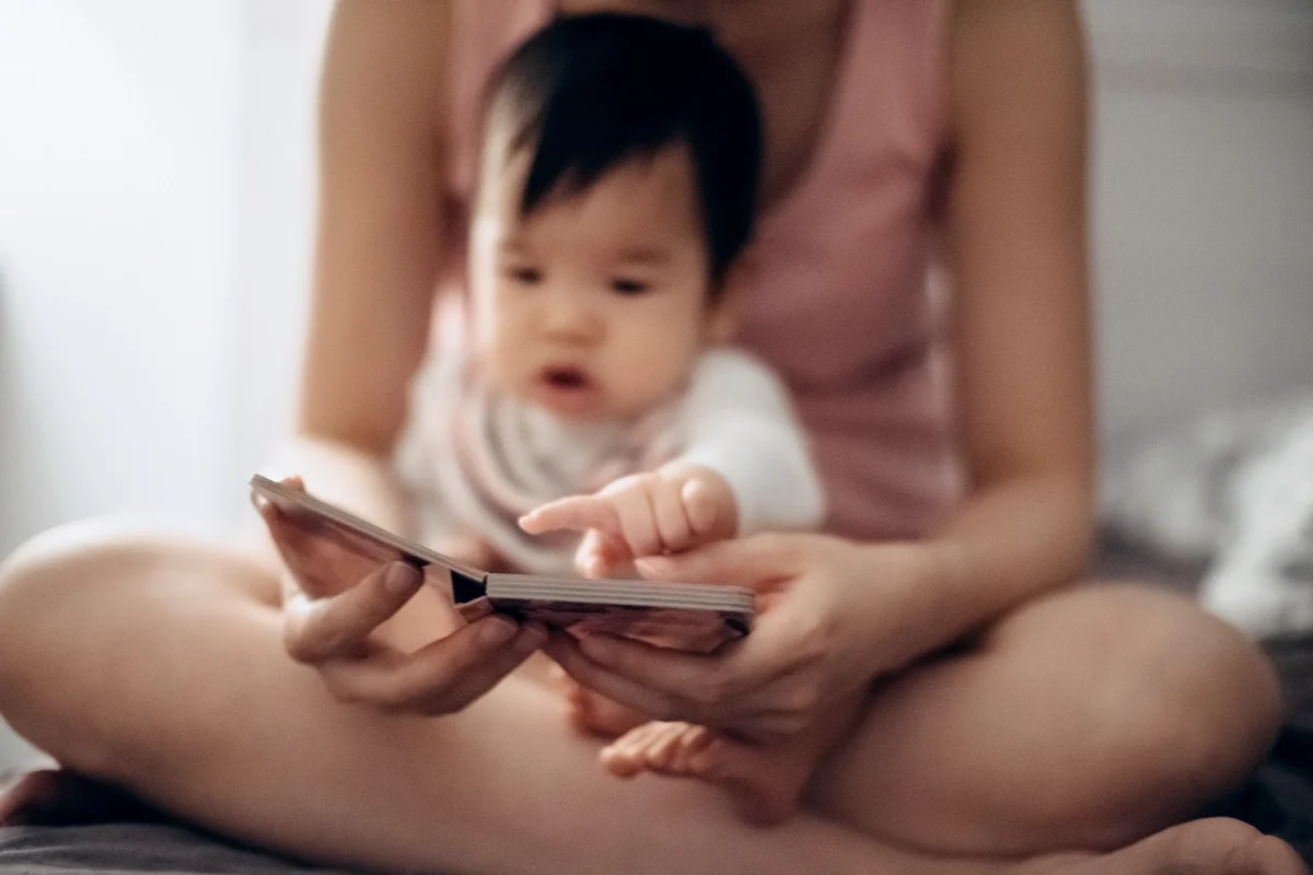 Baby sitting on mother's lap reading book in bed room before bed time