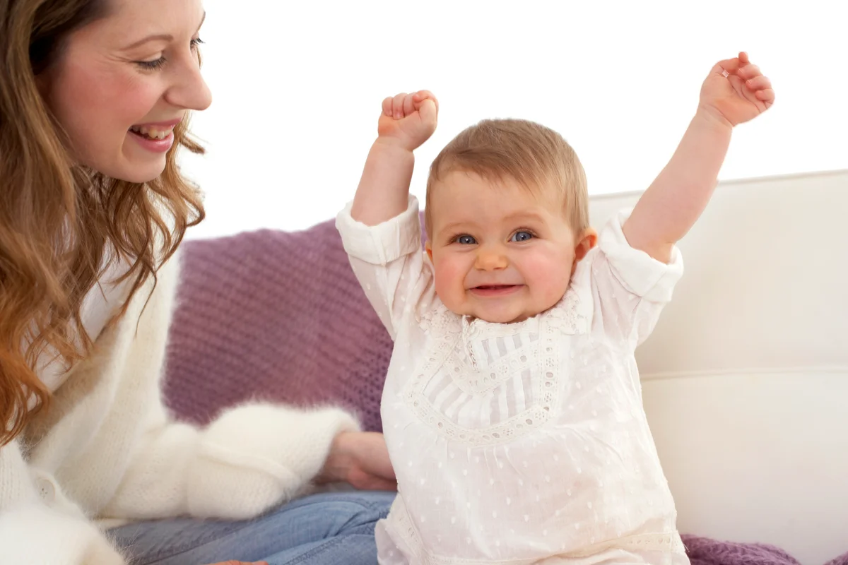 Smiling baby girl with outstretched arms beside her mother