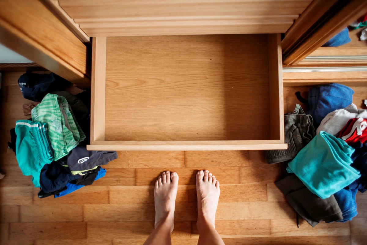 Empty dresser drawer and messy clothes all over the floor before organising