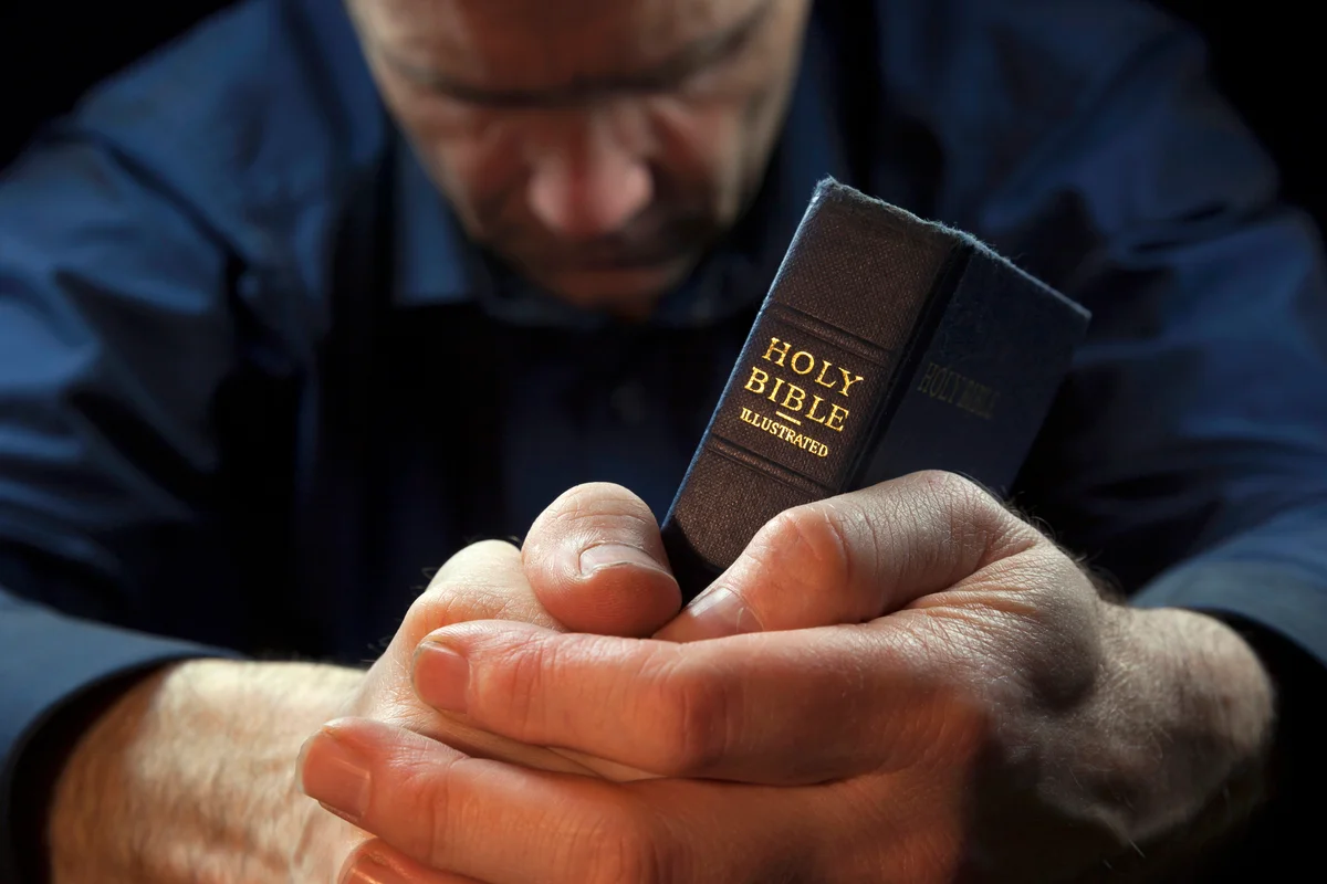 A Man praying holding a Holy Bible
