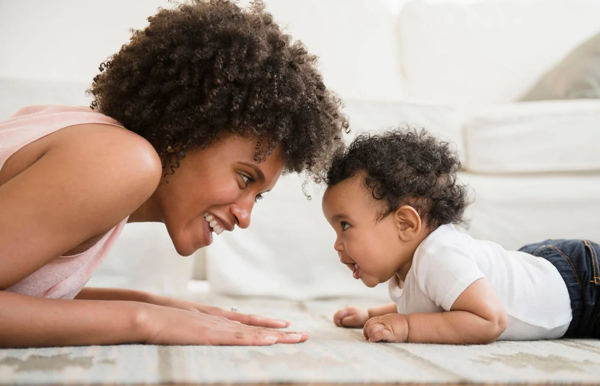 Mother playing face to face with baby son on floor