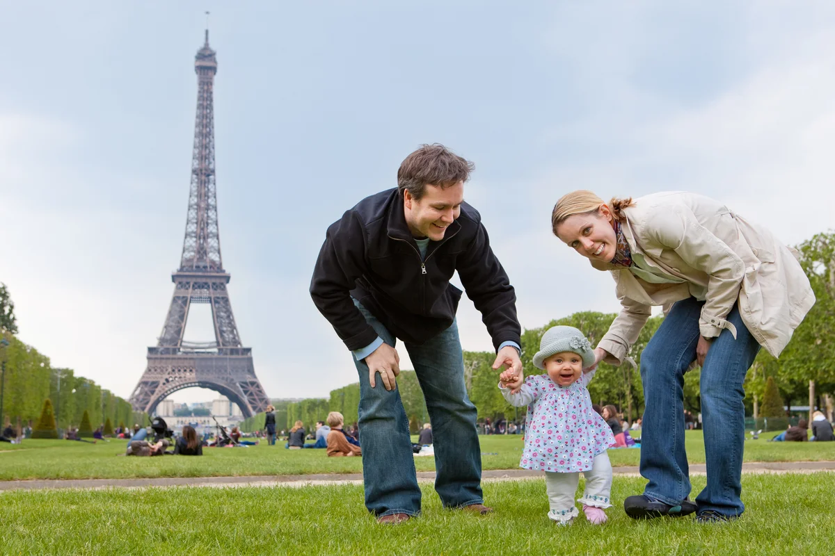 Young family with a baby visit Champ de Mars in front of the Eiffel tower in Paris