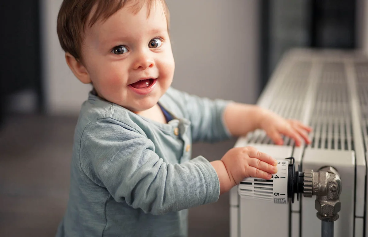 smiling baby boy playing with thermostat of heater