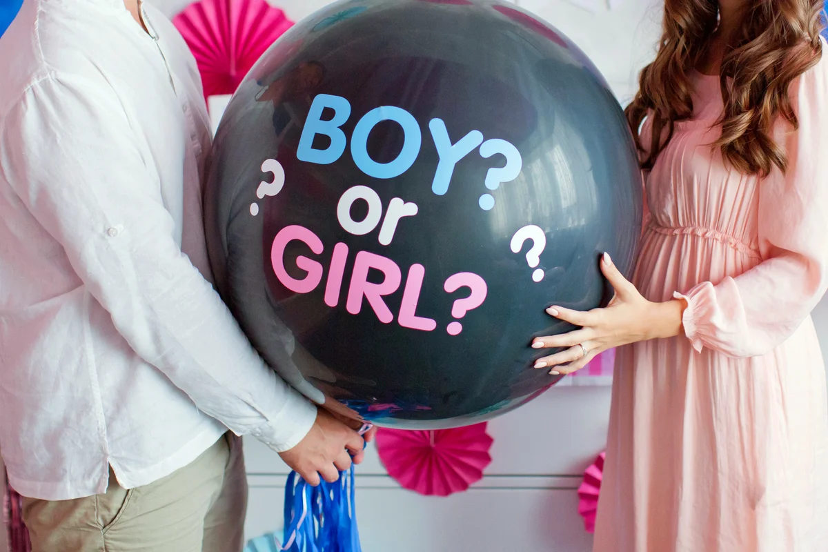 Man and woman holding black balloon with "boy or girl" on gender reveal party