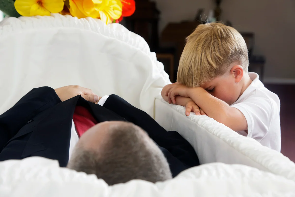 Sad little boy kneeling beside an open casket at a funeral