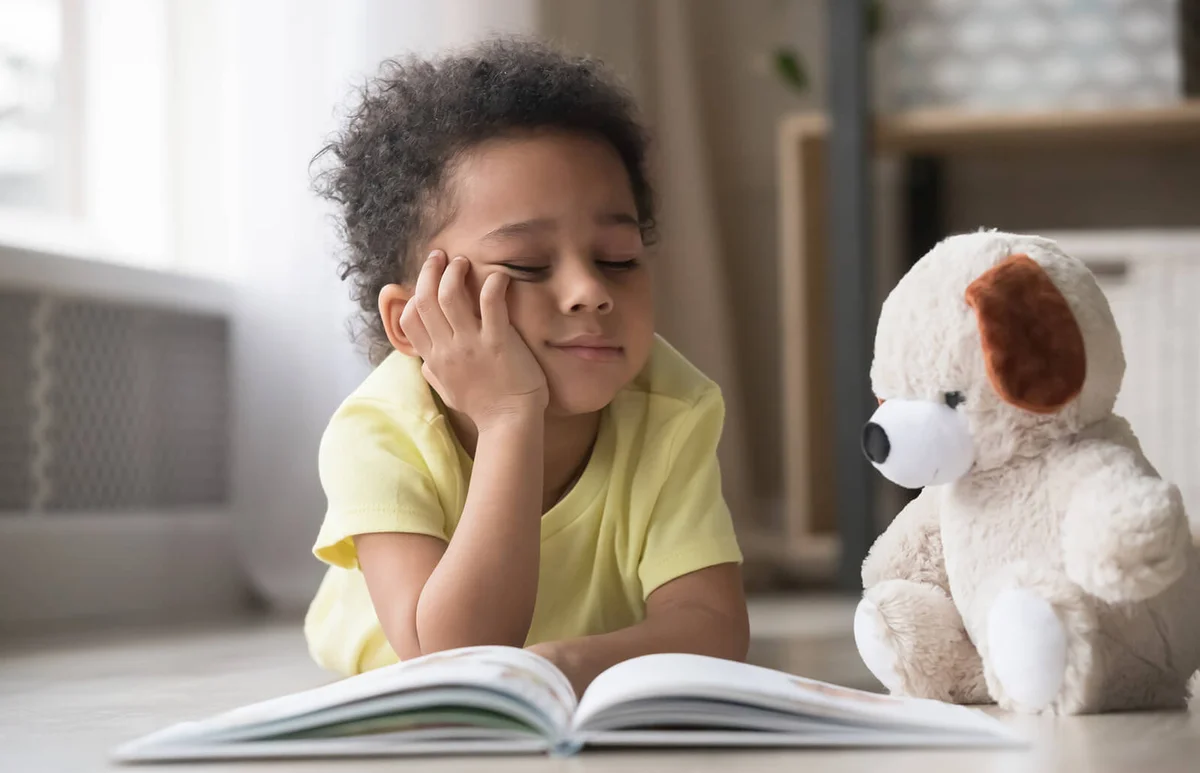 Bored little boy reading book lying on floor