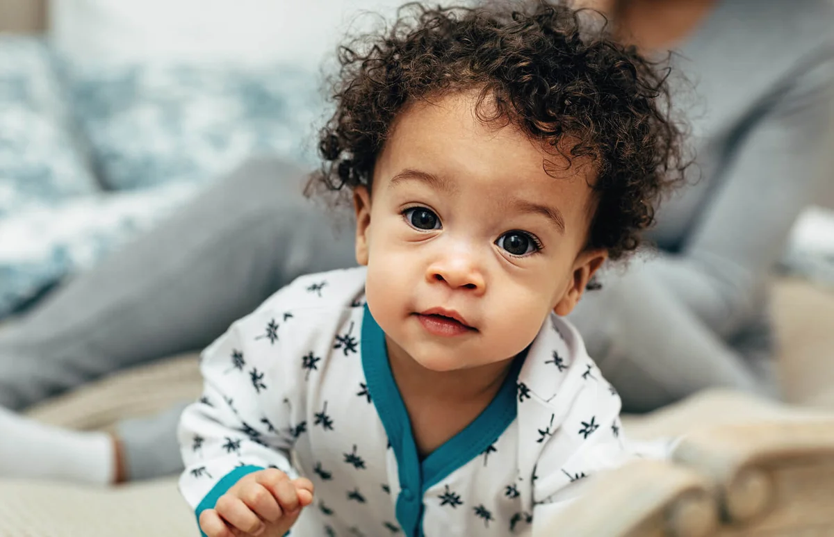 portrait of a curly-haired baby boy crawling on bed