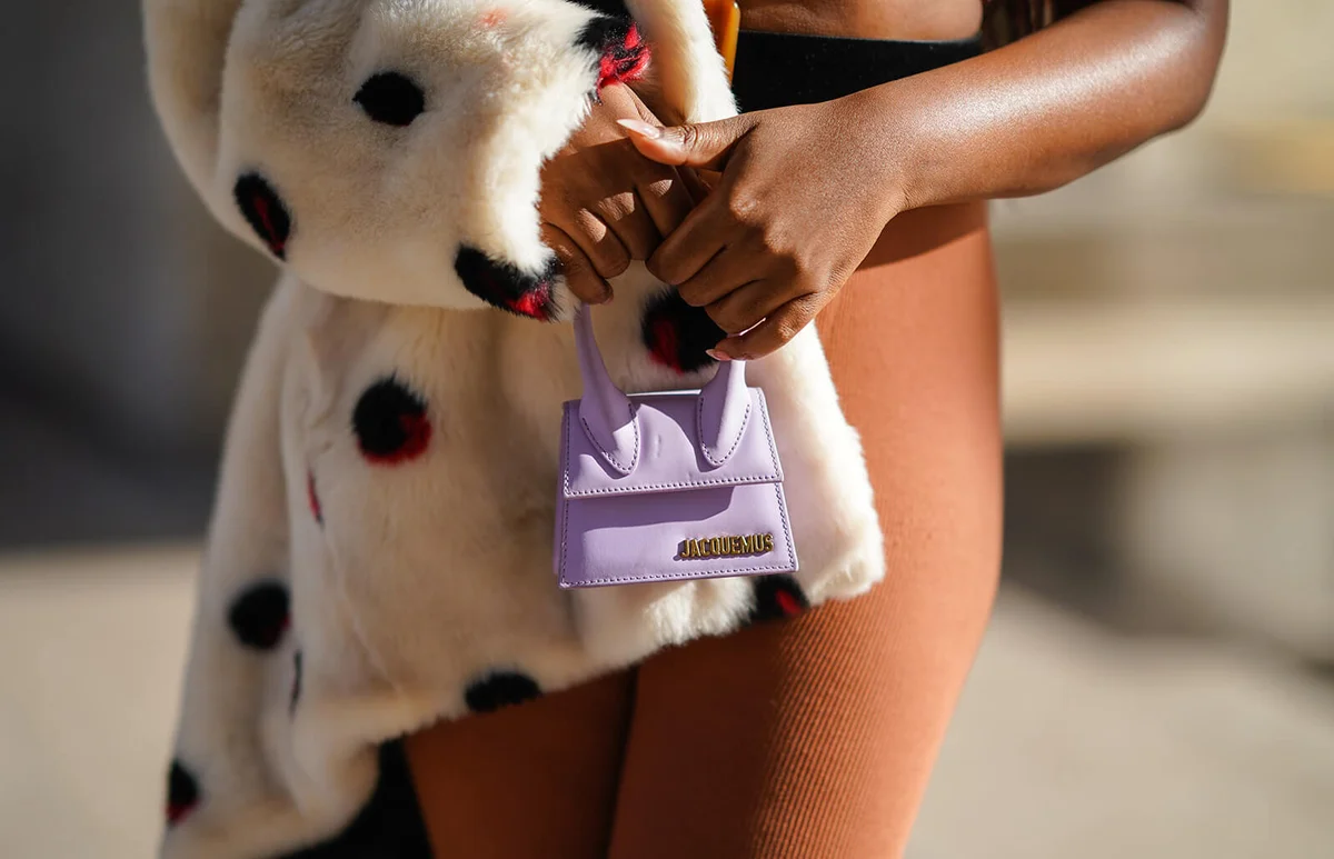 Fatou N'Diaye wears a white fluffy faux fur winter coat with printed large red and black dots from Eleven Paris, a pale purple mini Jacquemus bag | Getty Editorial Use
