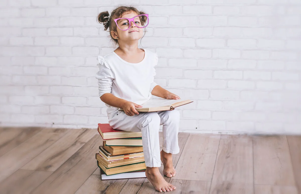 Child little girl sitting on a stack of books with glasses