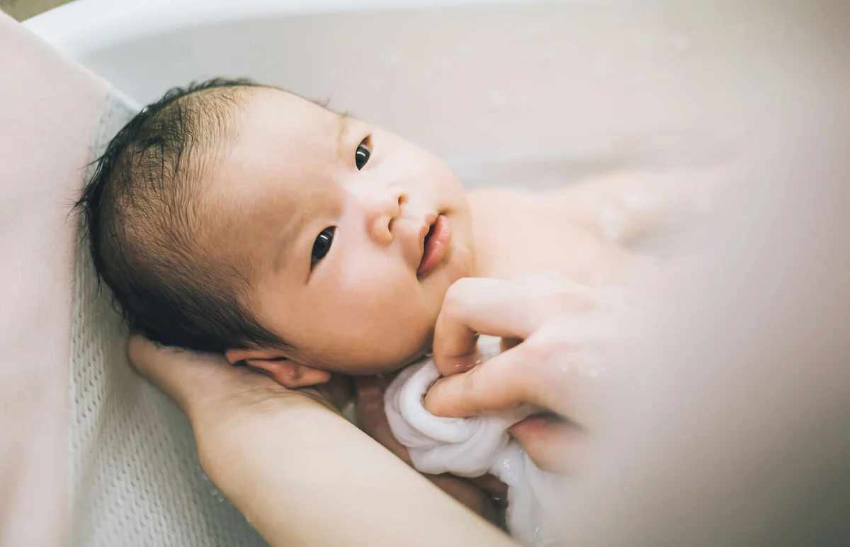 Mother bathing smiling new born baby in bathtub