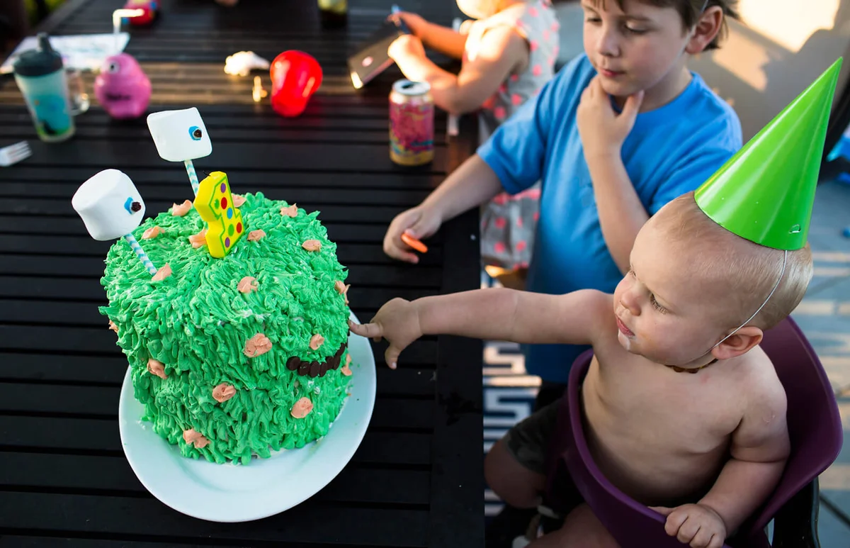 One Year Old Birthday Boy Wearing Green Party Hat Pokes Monster Cake