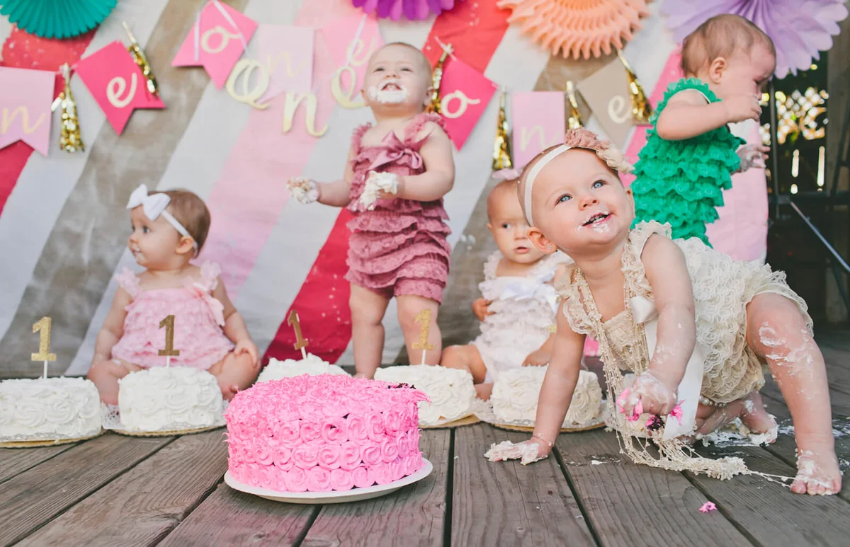 Cute baby girls with birthday cakes on floorboard at party
