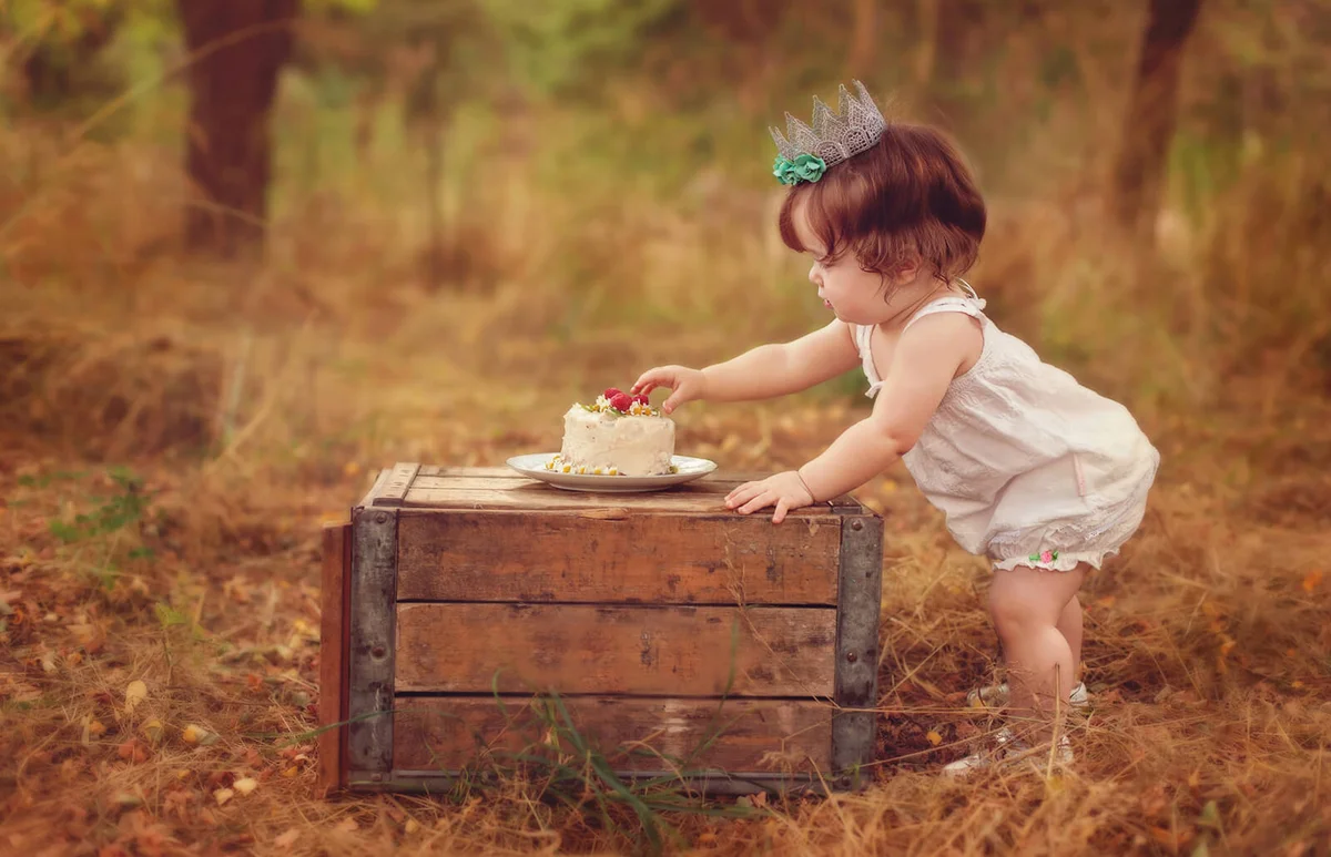 Little girl wearing a crown reaching for cake