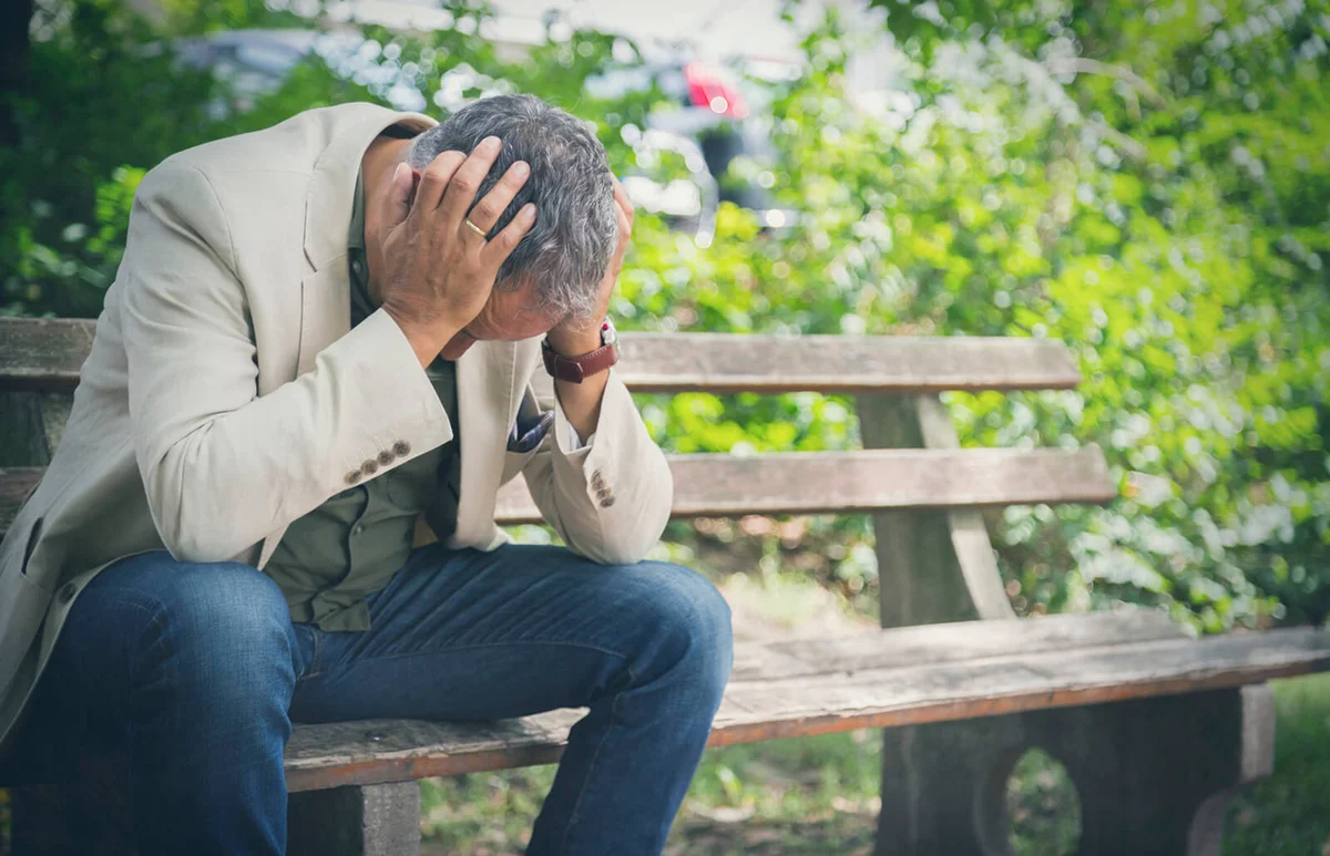 Man with head in his hands sitting on park bench