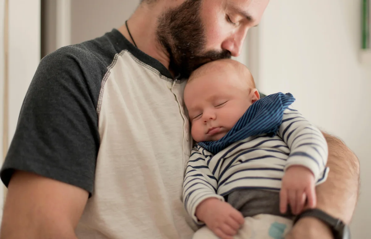 father kisses sleepy newborn