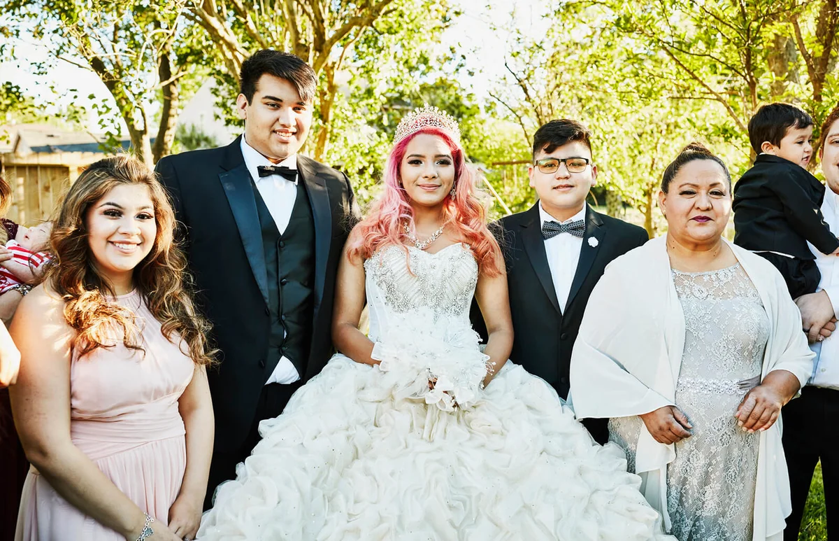 Young woman dressed in quinceanera gown standing in backyard surrounded by family