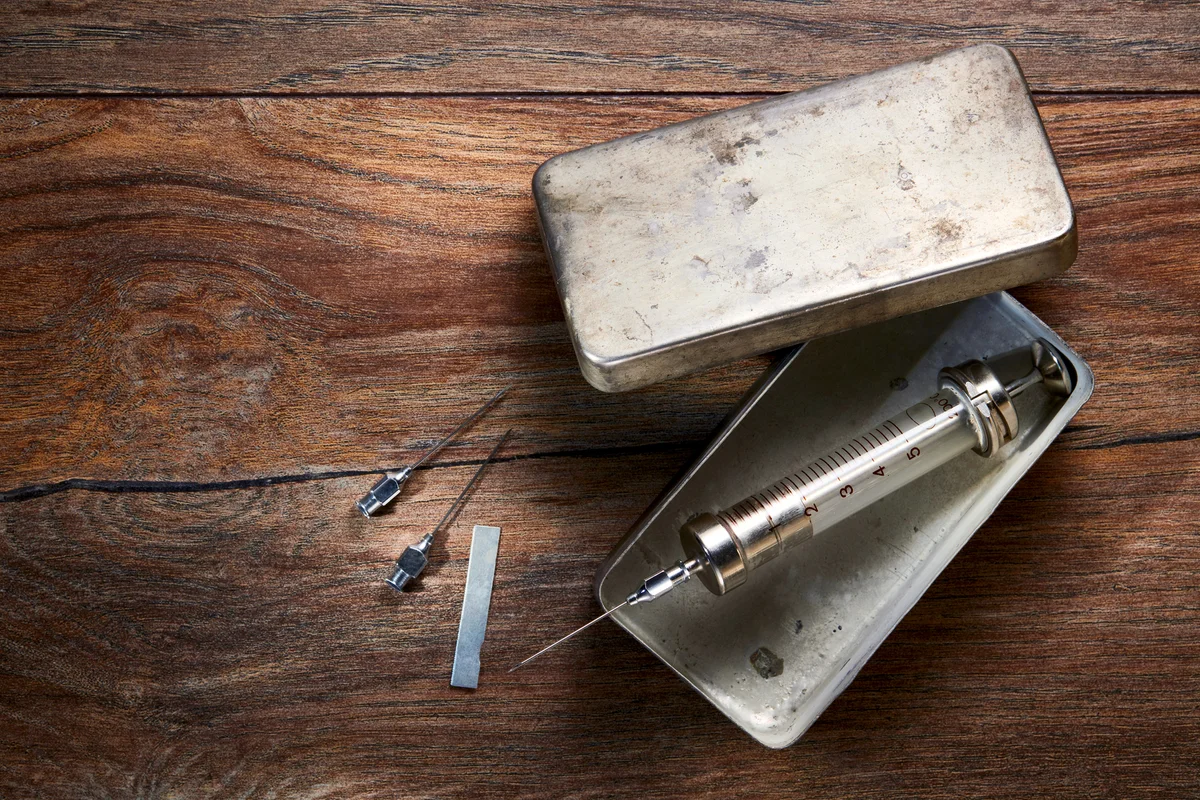 Vintage glass syringe in a metal box and needles on wooden table