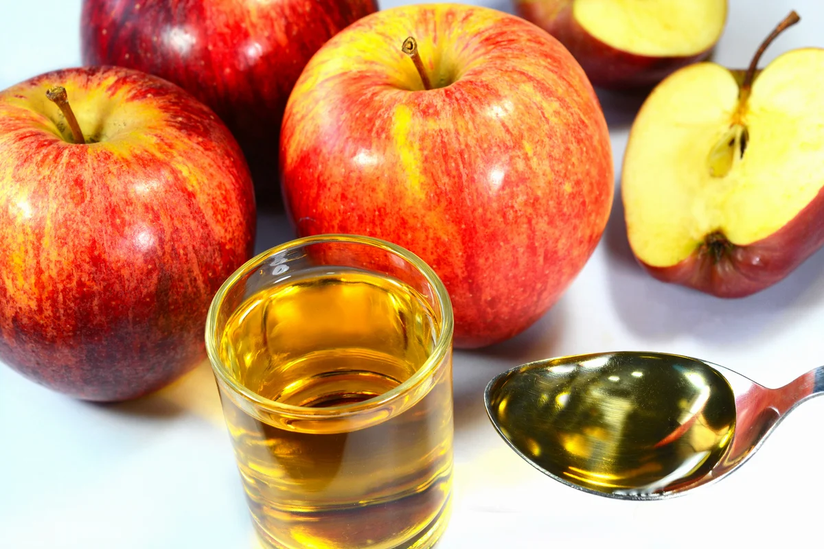 Apple cider vinegar in a cup and spoon with red apples on the background