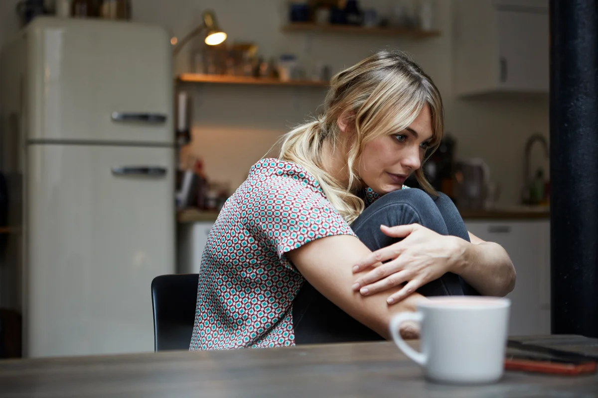 Woman looking sad and sitting alone in kitchen