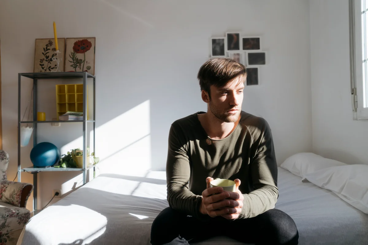 Man looking sad sitting on bed alone in house