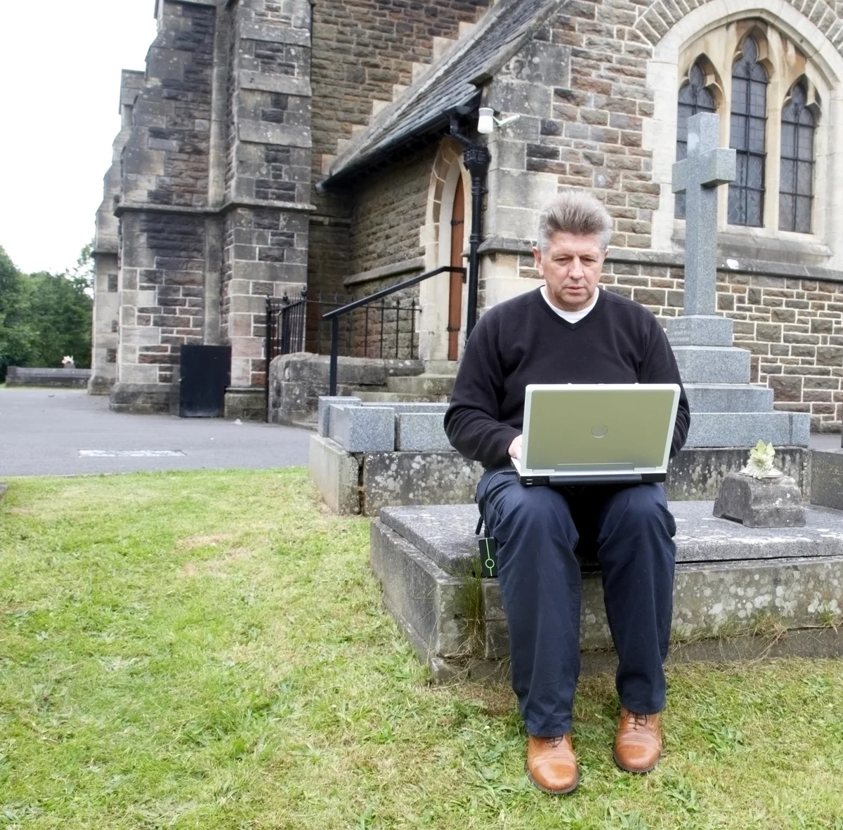 Man  sitting in a church cemetery while using a laptop