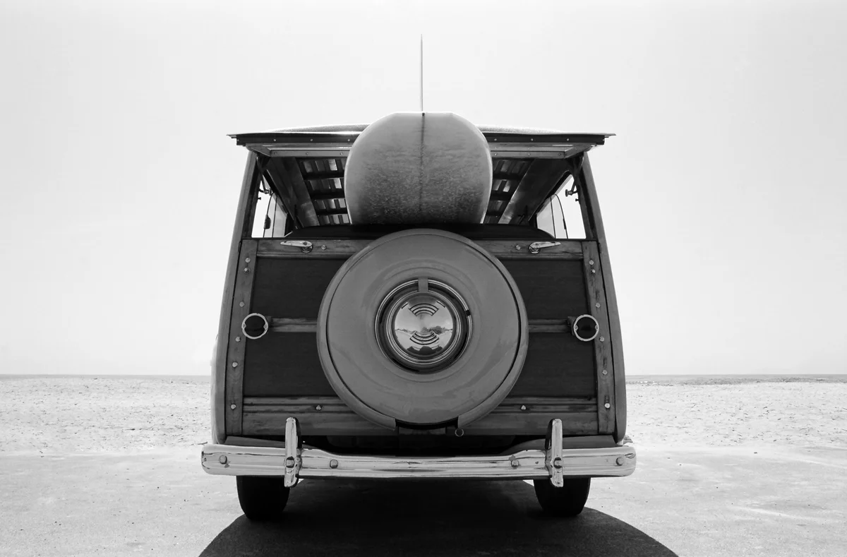 Old Woodie station wagon with surfboard at beach
