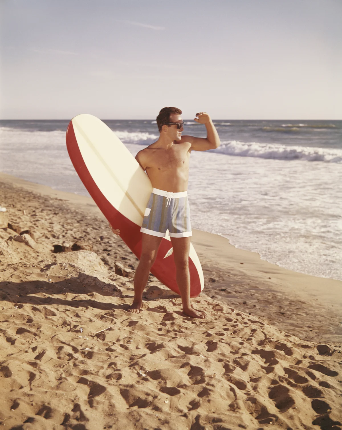 Retro art surfer holding surfboard while standing on beach