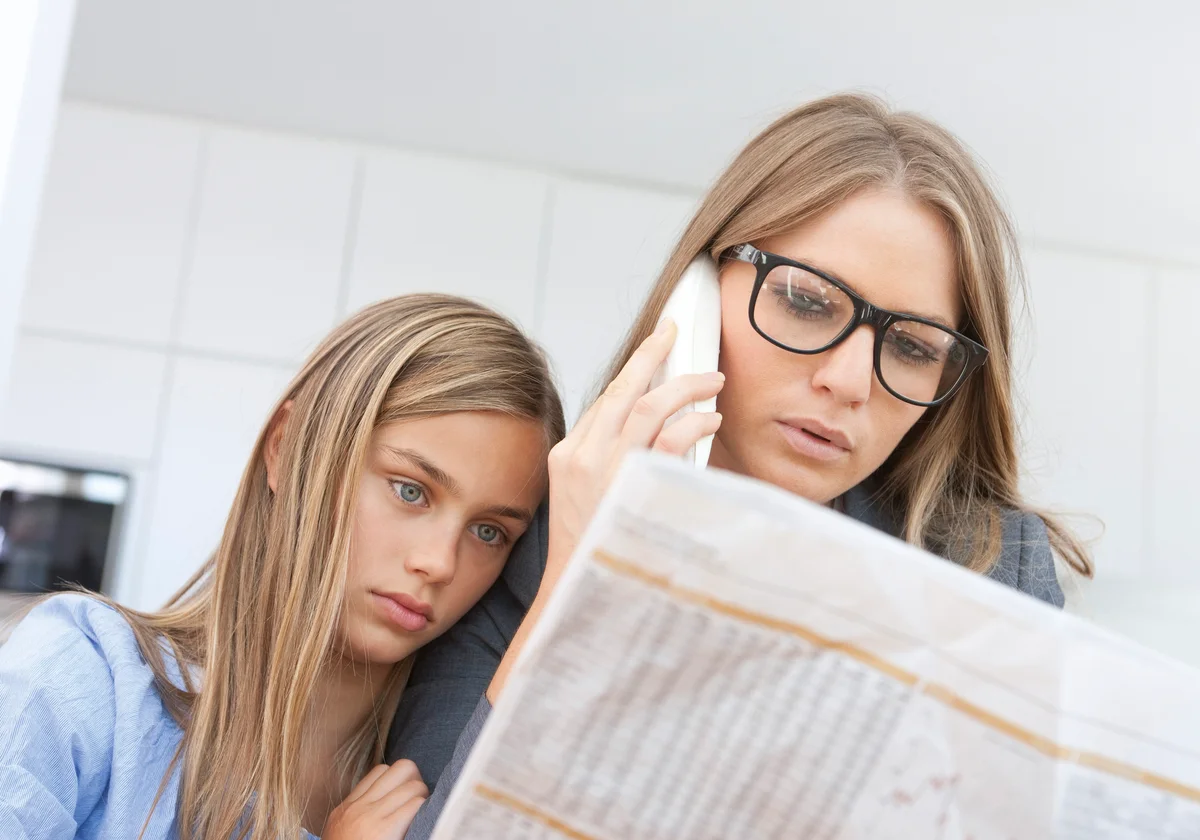 Mother and daughter reading newspaper and making a phone call