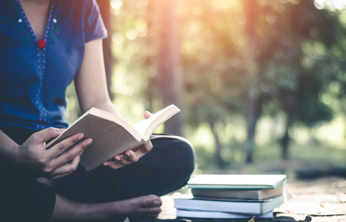 Woman Turning Book Pages While Sitting On Field