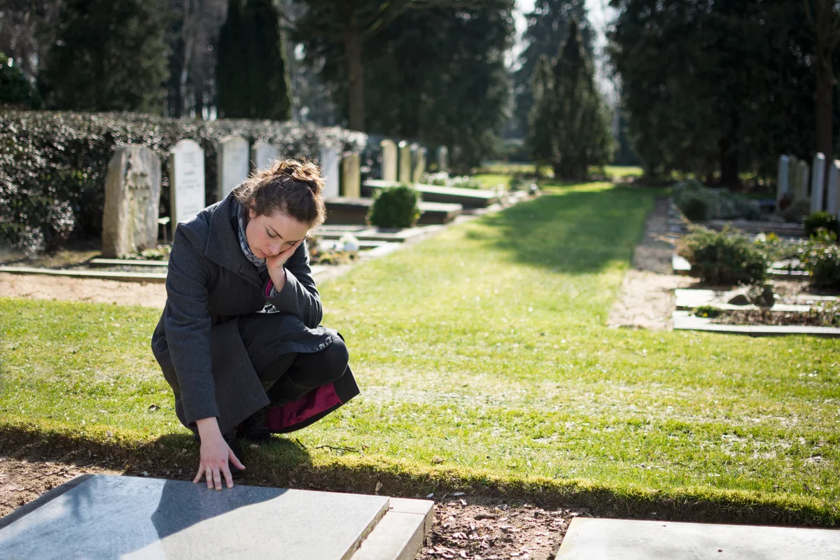 Sad woman lovingly touching gravemarker