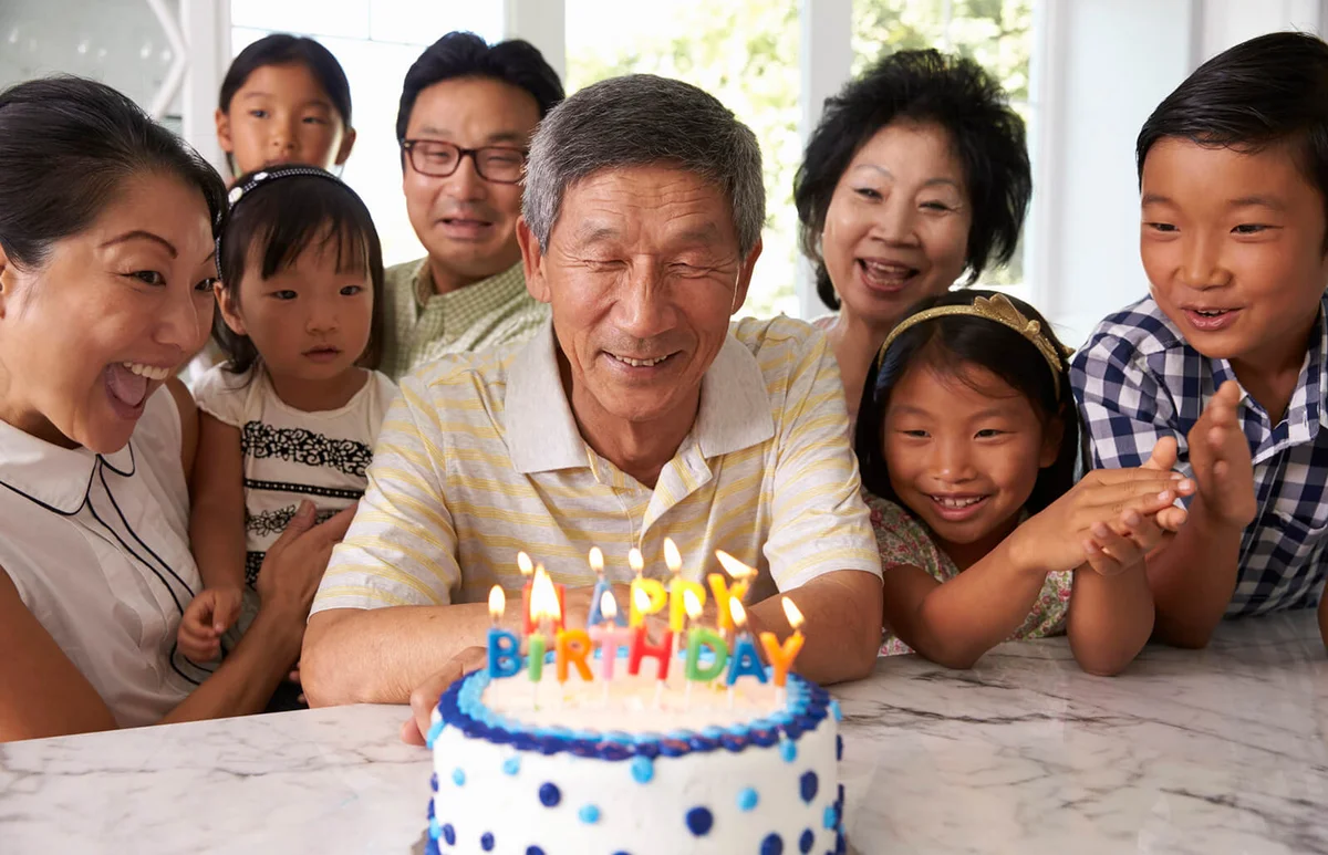 Grandfather Blows Out Candles On Birthday Cake