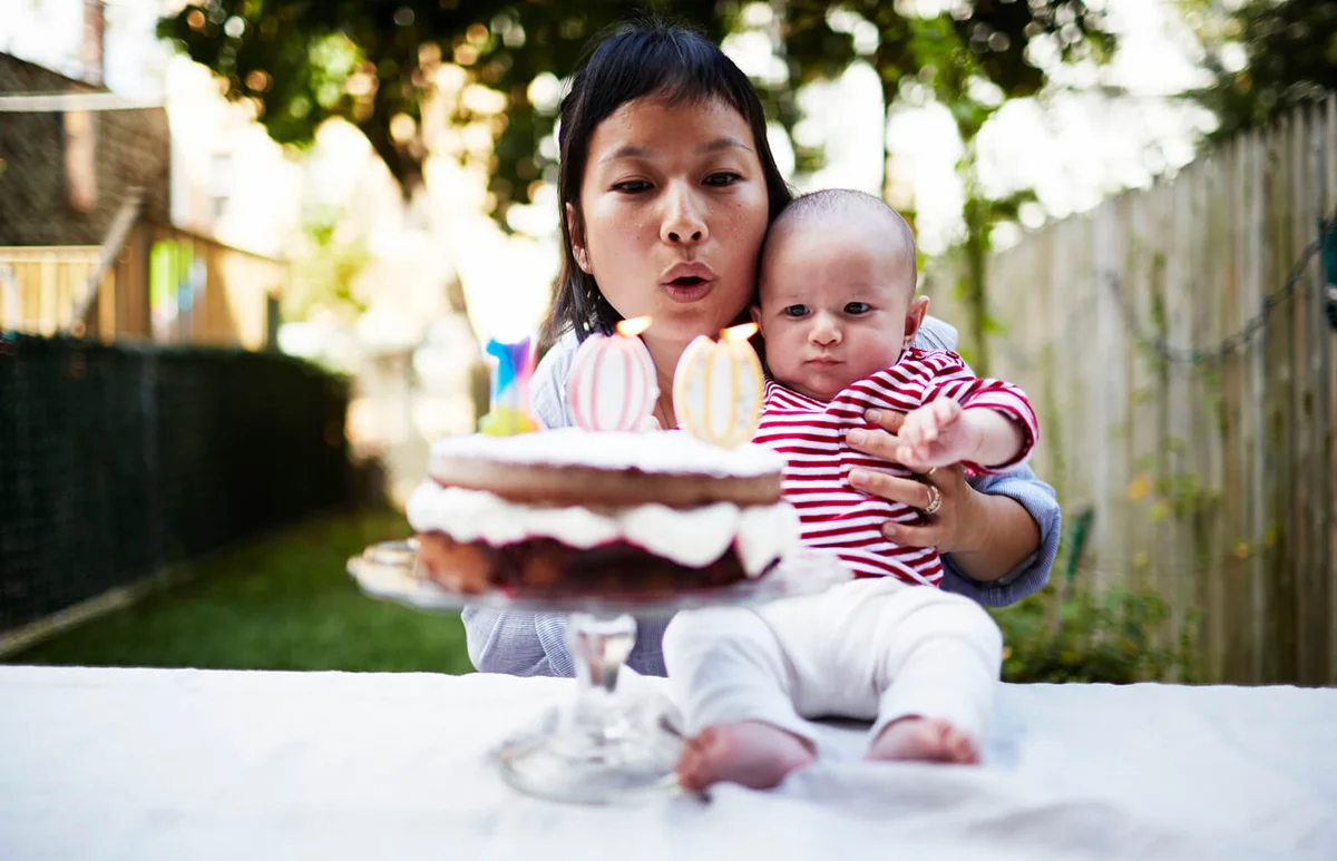 Mother holding baby son, blowing out candles on cake