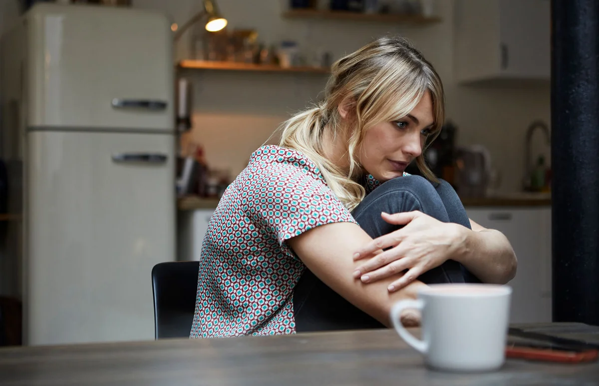 pensive woman sitting at table in the kitchen