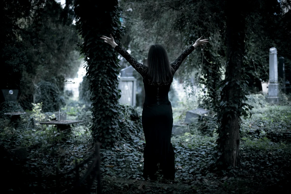 Young woman standing in an overgrown cemetery with hands stretched out