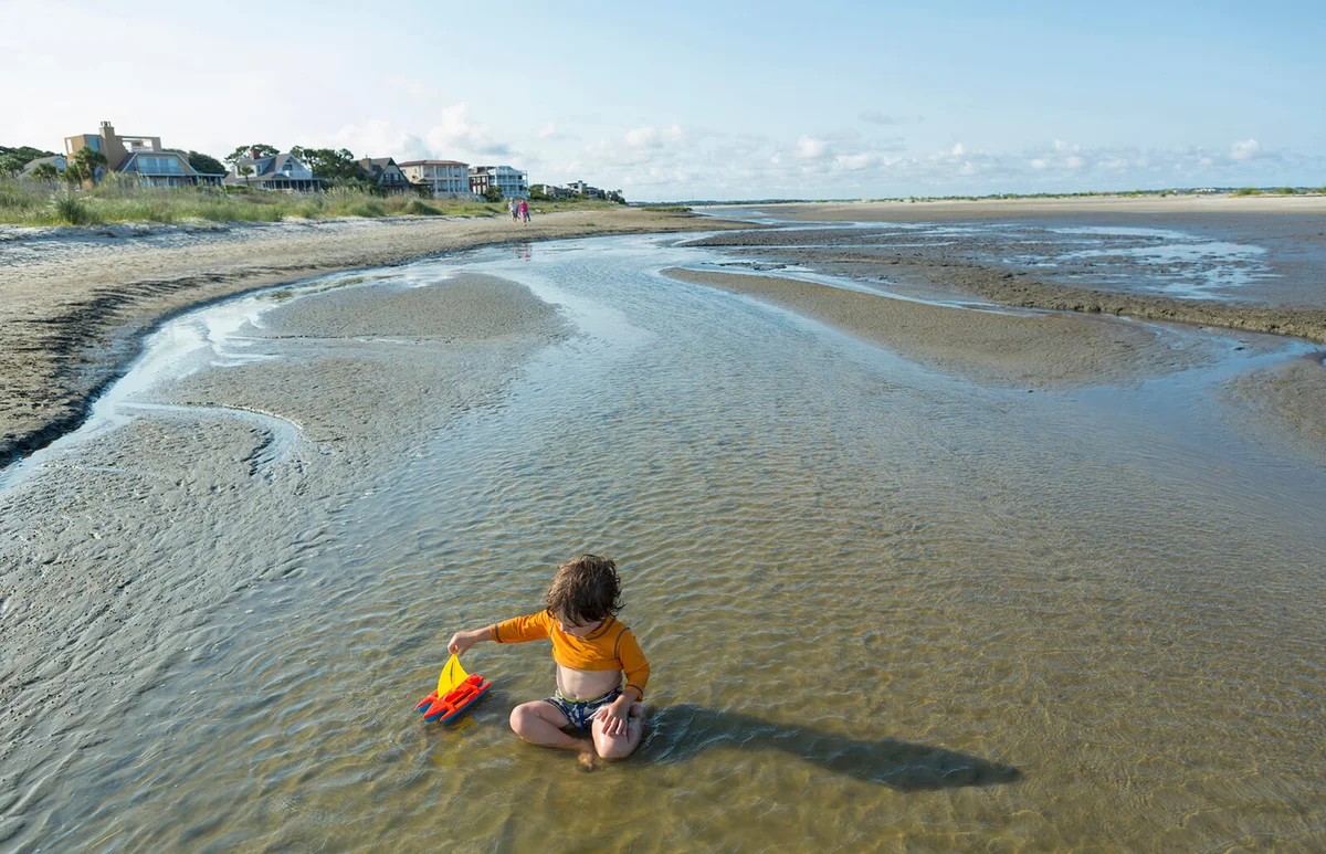 boy playing with sailboat in waves on beach